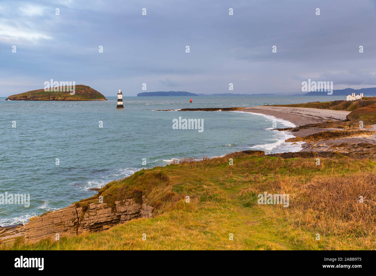 Faro Penmon (Trwyn Du Faro) sull'estremità orientale di Anglesey con Puffin Island (Ynys Seiriol) nella distanza dalla cima di una scogliera Foto Stock