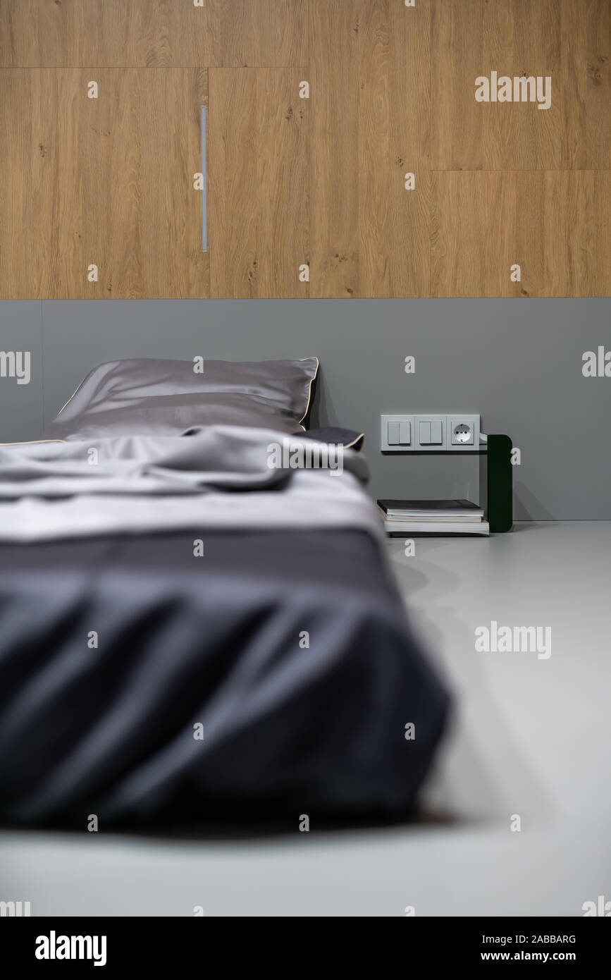 Fantastico posto letto con lenzuola di seta sul pavimento grigio nel luminoso interno con pareti in legno. Accanto ad essa ci sono libri, presa di alimentazione con sw Foto Stock