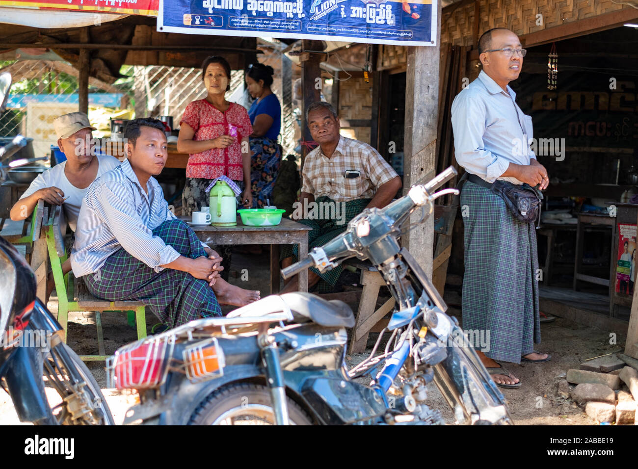 Popolo birmano in abito tradizionale di guardare un corteo nuziale mentre vi rilassate in un paese limitrofo di cafe vicino Monywa, Myanmar (Birmania) sul Fiume Chindwin Foto Stock