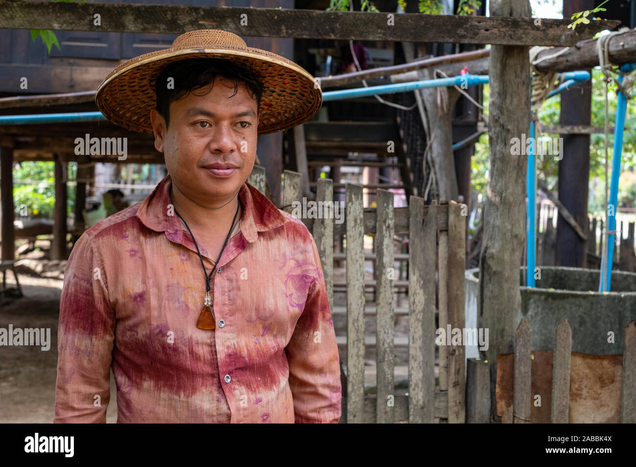 Un uomo maturo si erge al di fuori di casa sua che indossa una collana di ambra in un villaggio rurale nel nord-ovest del Myanmar (Birmania) lungo il fiume Chindwin Foto Stock