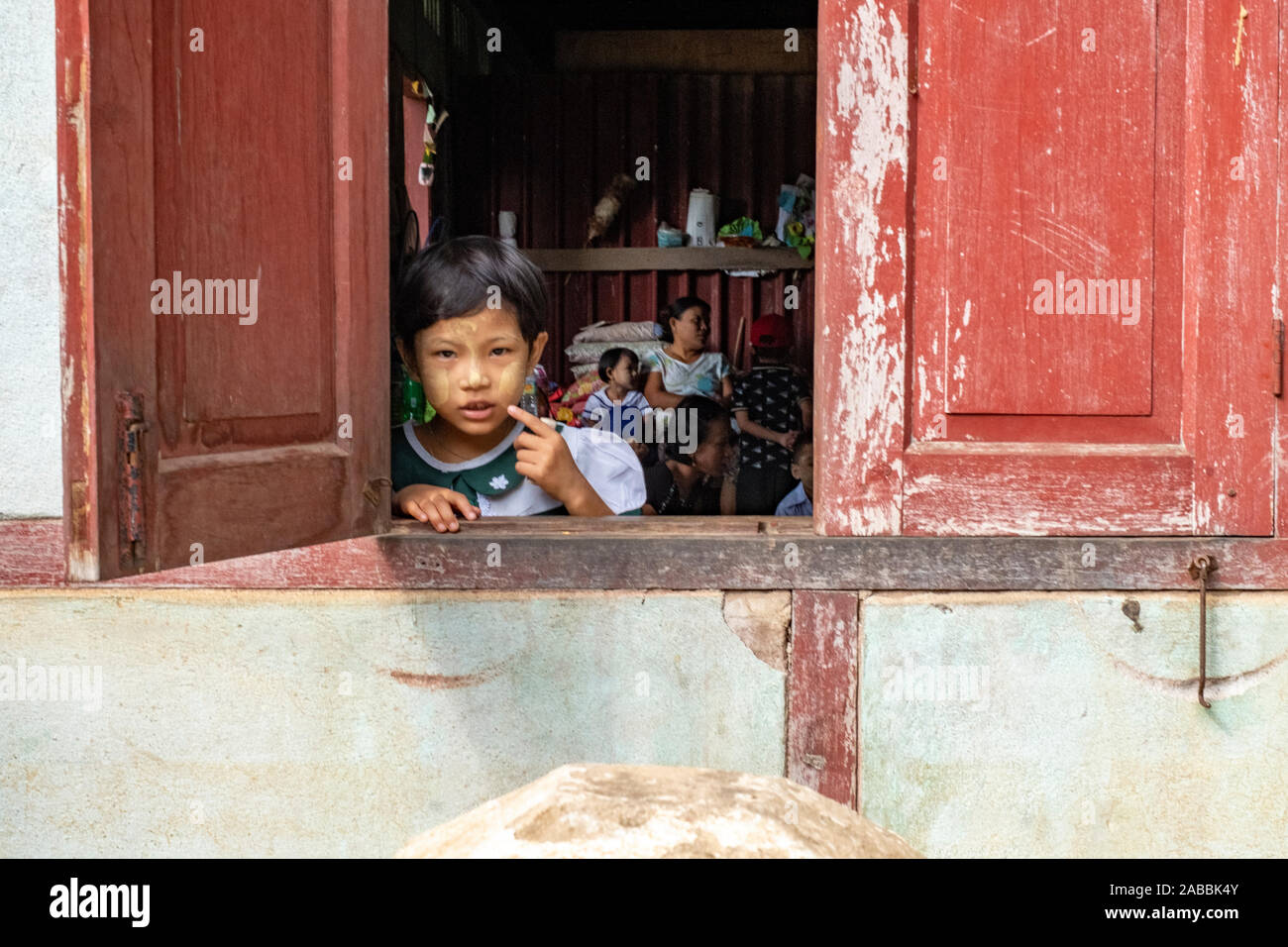 Una giovane ragazza si appoggia al di fuori della sua scuola elementare/kindergarten classroom finestra con curiosità in Kanne villaggio sul fiume Chindwin del Myanmar (Birmania) Foto Stock