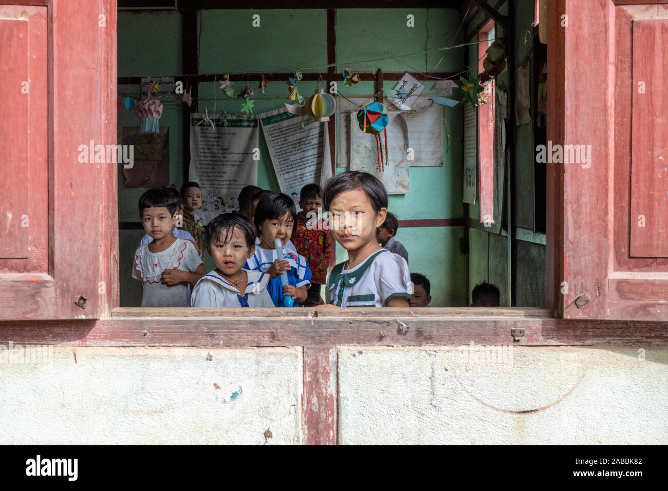 Gli studenti della scuola elementare lean al di fuori della loro classe finestra con sorrisi e curiosità in Kanne villaggio sul fiume Chindwin del Myanmar (Birmania) Foto Stock