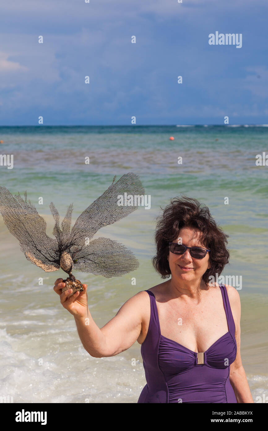 Donna matura in possesso di un quadro essiccato di un'alga su una spiaggia vicino a Tulum Messico Foto Stock