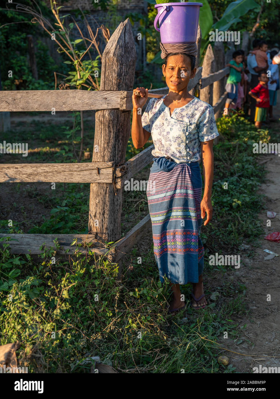 Donna matura porta una benna sulla sua testa come si ritorna a casa dopo una lunga giornata di lavoro lungo il fiume Chindwin nel nord-ovest del Myanmar (Birmania) Foto Stock