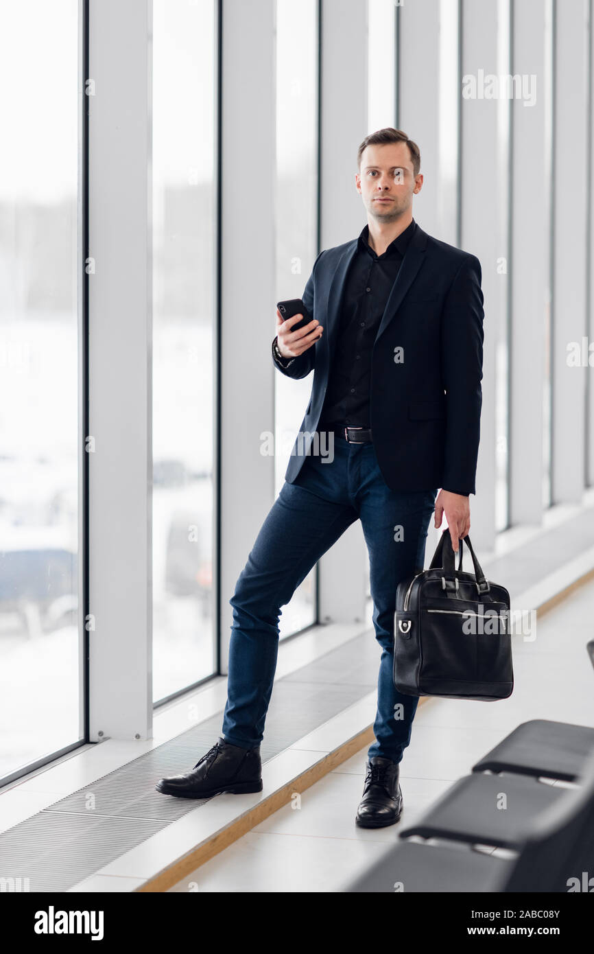Uomo d'affari tramite telefono mobile app in aeroporto. Giovane professionista business man texting a piedi dello smartphone all'interno di edificio per uffici o terminale di un aeroporto Foto Stock