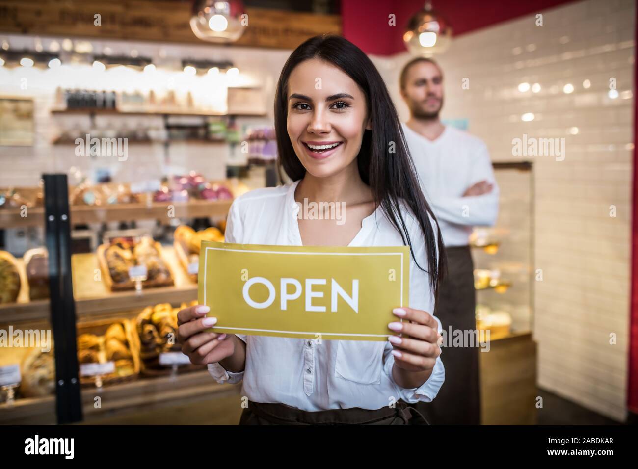 Donna che mantiene segno aperto durante l'apertura di pasticceria con marito Foto Stock