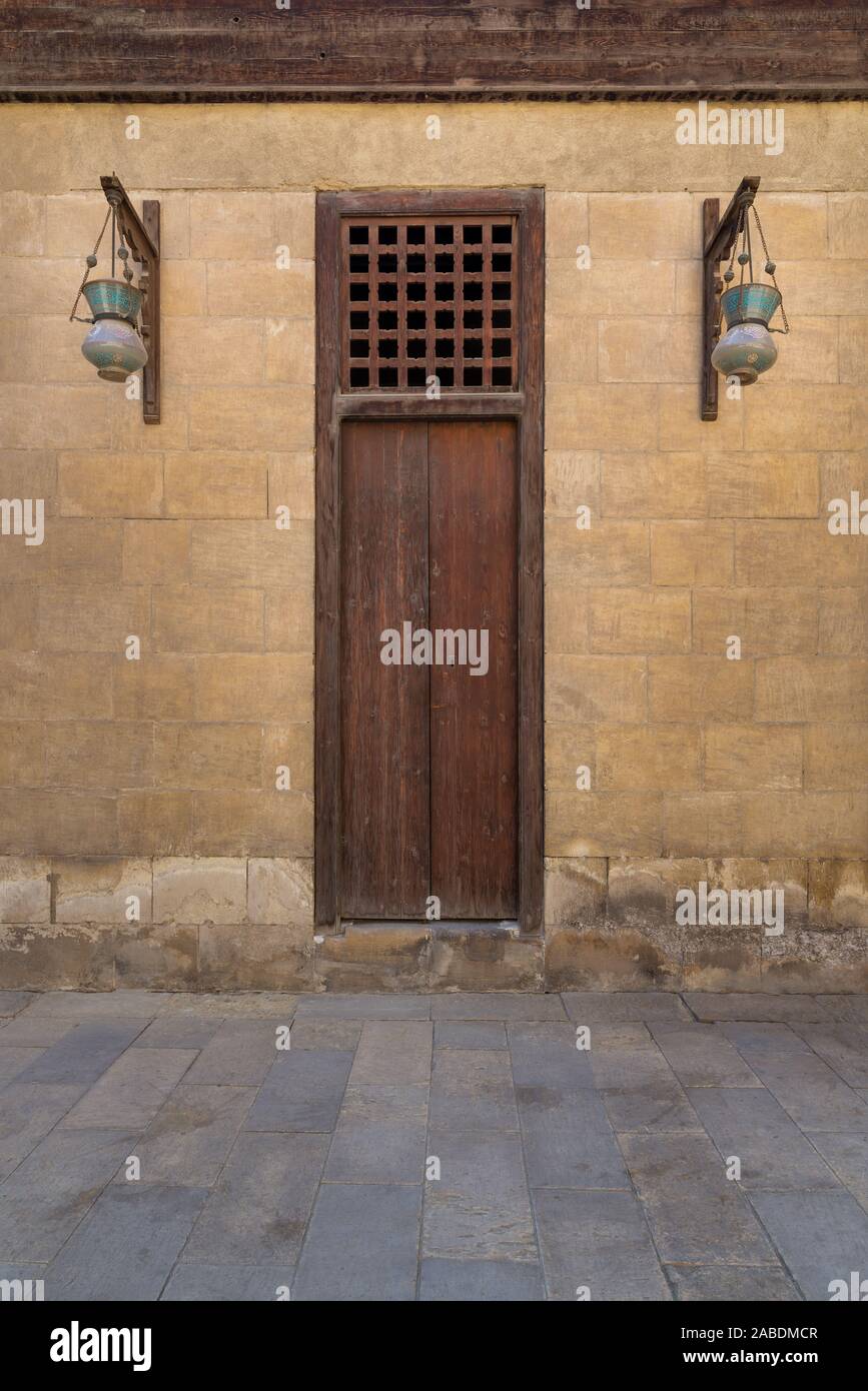 In legno porta chiusa e due arabo di vetro lanterne di strada impiccato su un palo di legno in antica pietra muro in mattoni, Cairo medioevale, Egitto Foto Stock