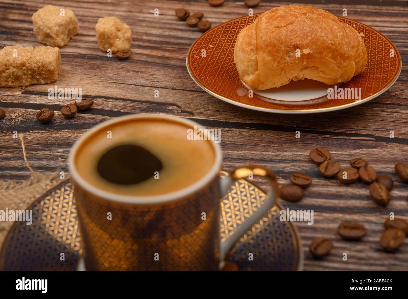 Tazza da caffè, croissant, lo zucchero di canna e i chicchi di caffè su sfondo di legno. Close up Foto Stock