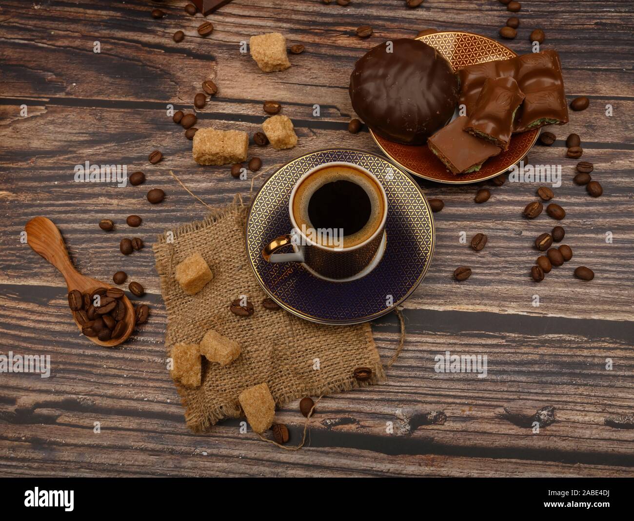 Una tazza di caffè, i chicchi di caffè e lo zucchero di canna, pezzetti di cioccolato, marshmallows in cioccolato su uno sfondo di legno Foto Stock