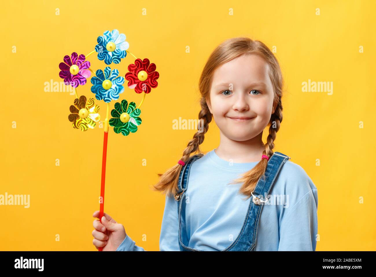 Carino felice bellissima bambina tenendo una girandola giocattolo. Bambino close-up su uno sfondo giallo. Foto Stock