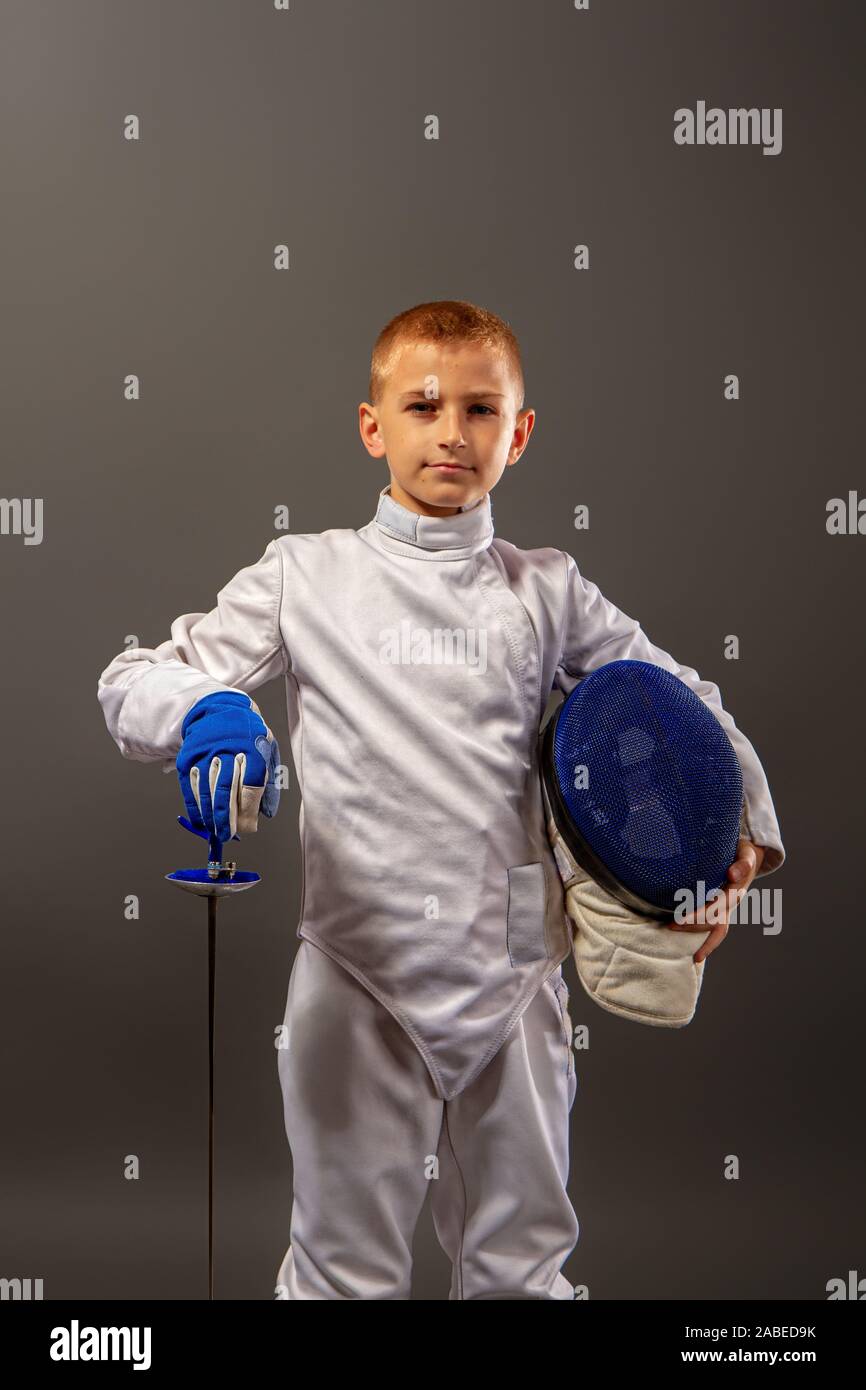 Little Boy fencer armati con una piattina di pinza in bianco le attrezzature sportive e di un casco protettivo su sfondo scuro Foto Stock