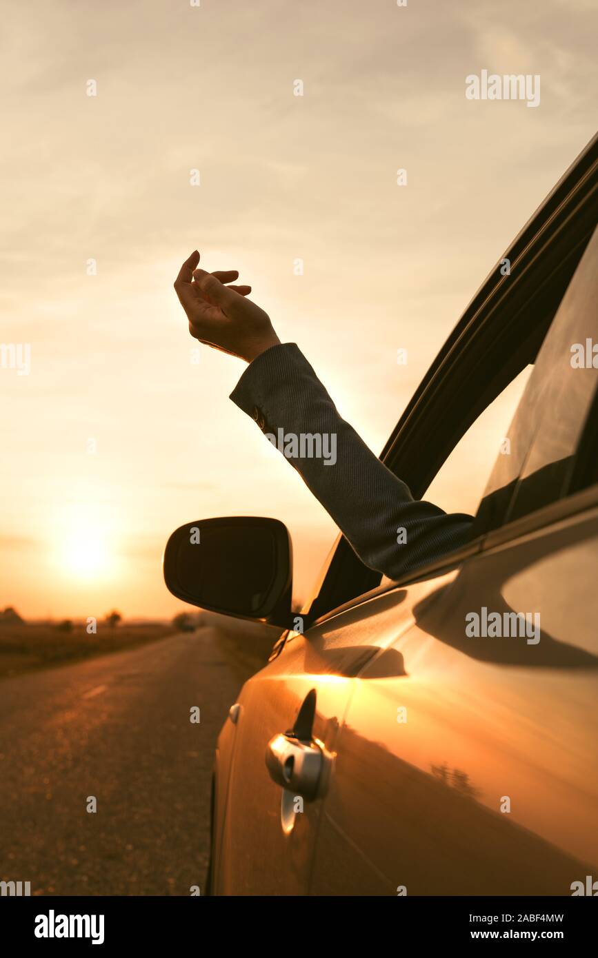 Sentire il vento mentre si guida attraverso la campagna, donna raggiungendo fuori mano dal finestrino in autunno il tramonto, il fuoco selettivo Foto Stock