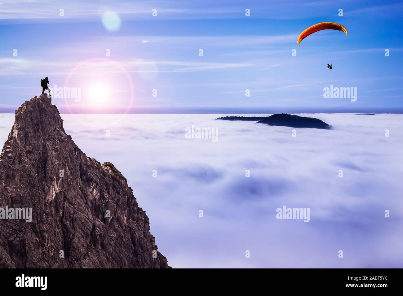 Escursionista presso la sommità di una roccia a guardare un parapendio al di sopra della copertura nuvolosa Foto Stock