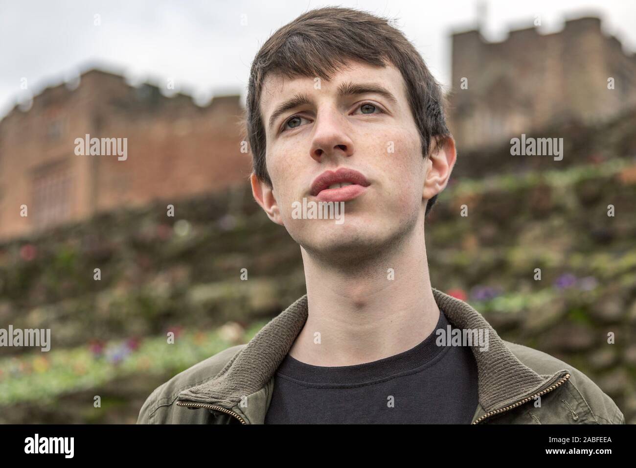 Un bel giovane uomo nel suo late adolescenti o poco più che ventenne sorge all'aperto e guarda a distanza con un promettente e pensieroso espressione. Foto Stock