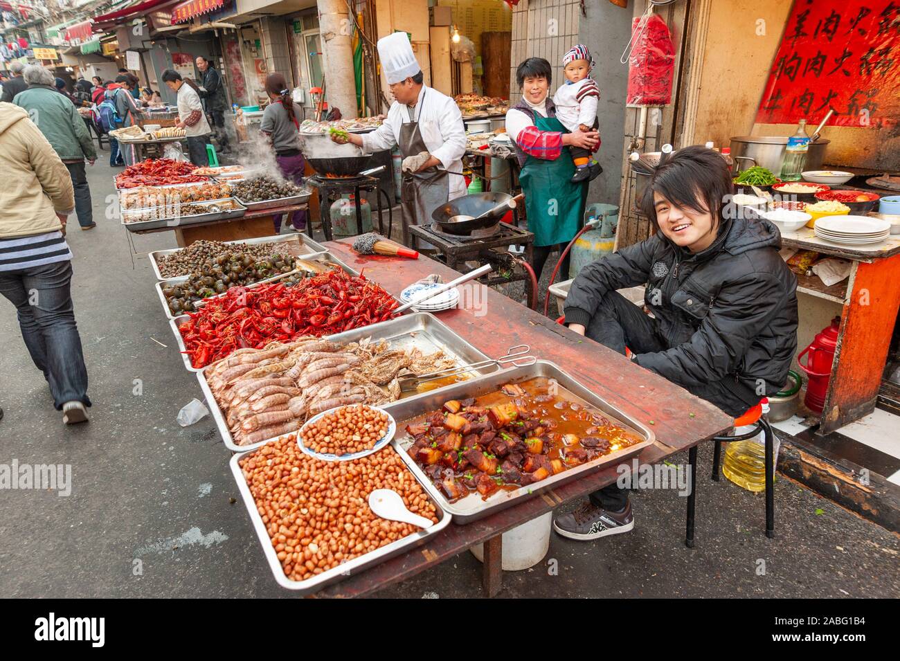 Aspirazioni di adolescente su i suoi genitori di stallo di mercato la vendita di cibo di strada nella città vecchia, Shanghai, Cina Foto Stock