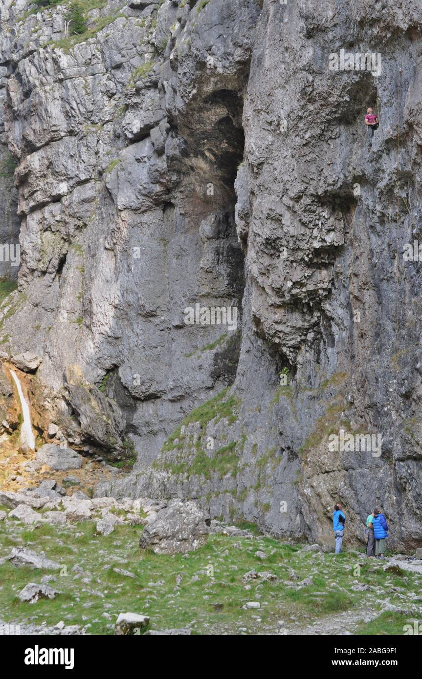 Malham Cove,Skipton, Yorkshire/Regno Unito 11 Settembre 2014: una persona salire la Malham roccia durate tre altri guardano da sotto. Foto Stock