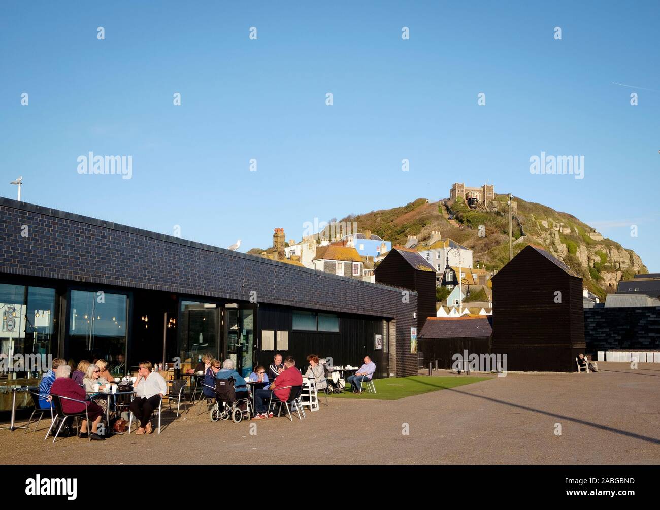 La gente seduta al di fuori del Stade cafe / ristorante sul lungomare di Hastings con East Hill in background Foto Stock