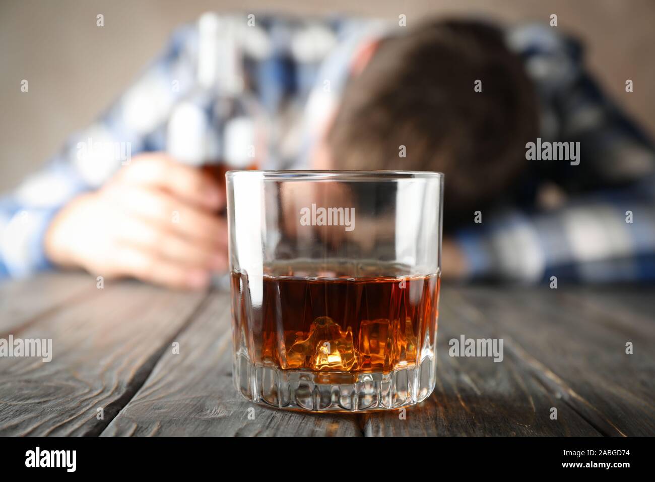 Bicchiere di whiskey contro uomo ubriaco su sfondo di legno, close up Foto Stock