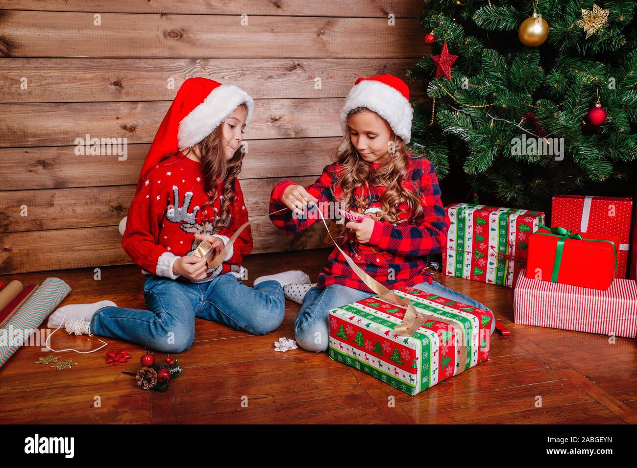 Felice di due bambine in cappelli di Babbo Natale pack doni vicino albero  di Natale Foto stock - Alamy