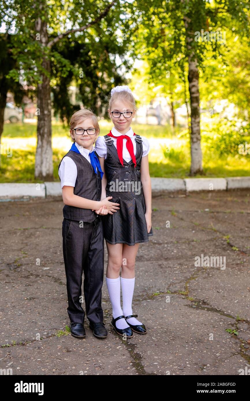 Una scolaretta in una camicia bianca con una cravatta rossa, con un inchino  e il suo piccolo fratello con cravatta blu e glasse nella classe. Si torna  a scuola concetto Foto stock -