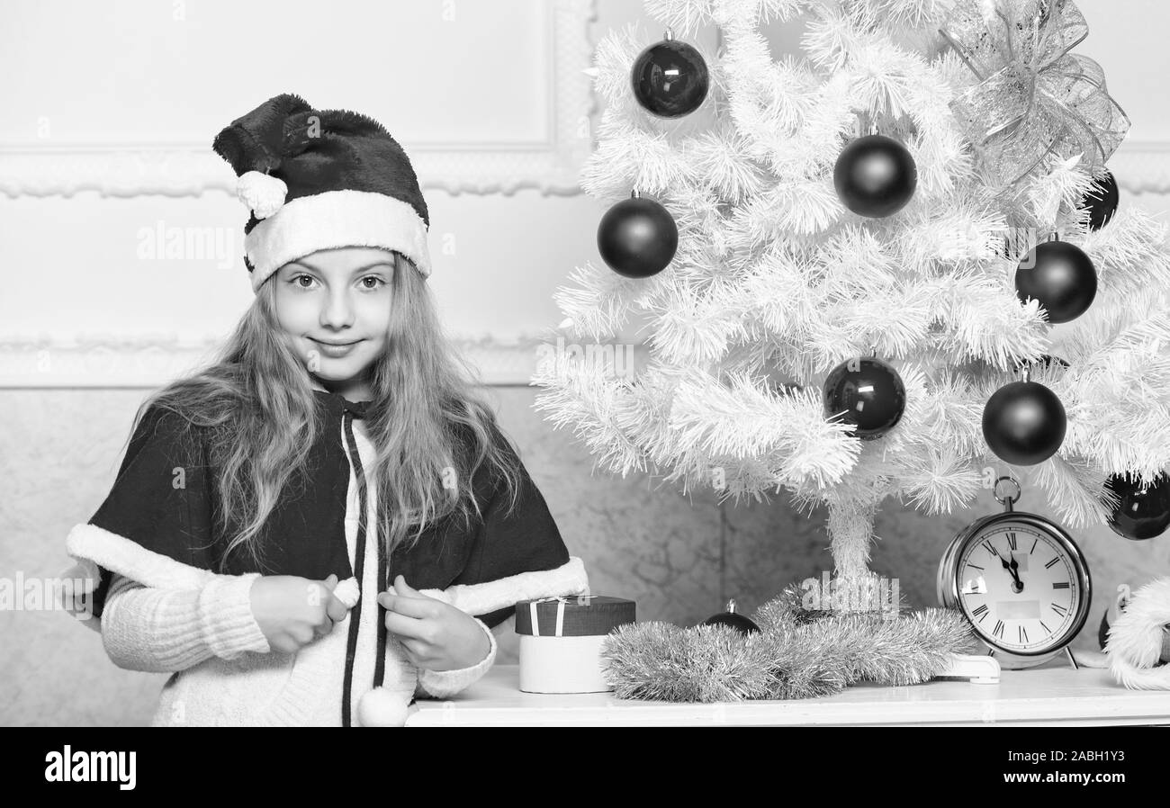 Cherished holiday attività. Capretto in santa hat decorare albero di natale. La tradizione di famiglia concetto. Bambino la decorazione di albero di natale con palline rosse ornamenti. Ragazza kid decorare albero di natale. Foto Stock