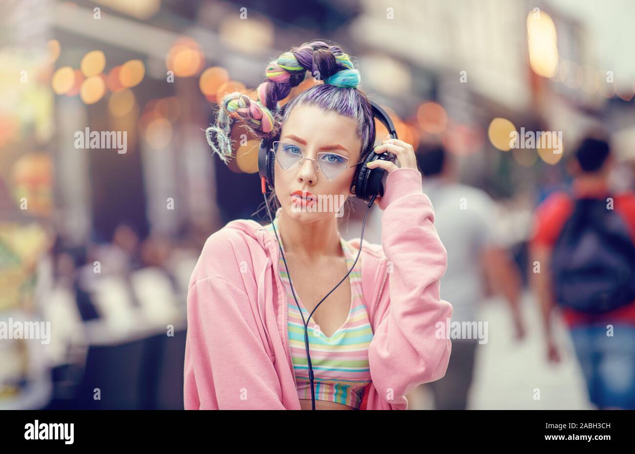 Urban Ritratto di una giovane donna nonconformista modello. Ragazza ascoltando la musica nelle cuffie su strade affollate. Vanguard moda. Avantgarde. Foto Stock