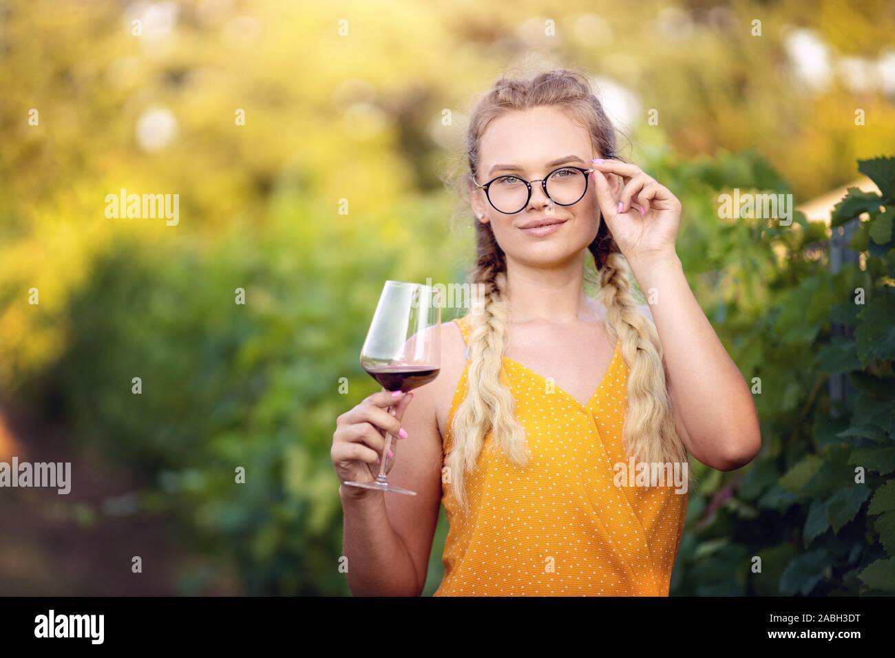 Ritratto di una bella donna bionda con gli occhiali gustando un bicchiere di vino rosso. Solo ponendo femmina e fare un brindisi all'aperto Foto Stock
