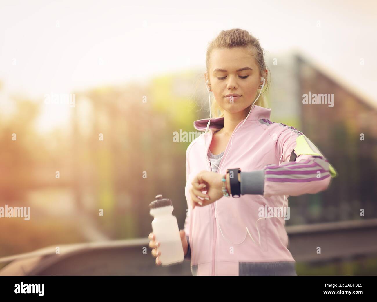 Runner acceso al tramonto nel parco della città - sano donna fitness jogging all'aperto - atleta ascoltare musica durante l'allenamento al parco e adjustin Foto Stock