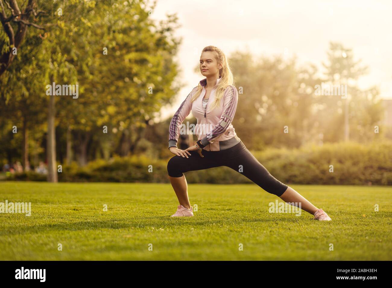 Giovane donna stretching e riscaldamento fino a park durante il tramonto - attraente ragazza prima di fitness in autunno park Foto Stock