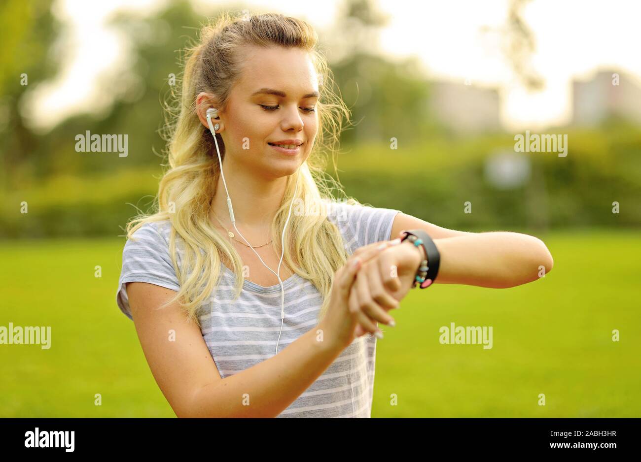 Giovane atleta ascoltare musica durante l'allenamento al park e l'impostazione smart watch - Giovane donna regolazione della smartwatch prima di attività sportiva in th Foto Stock