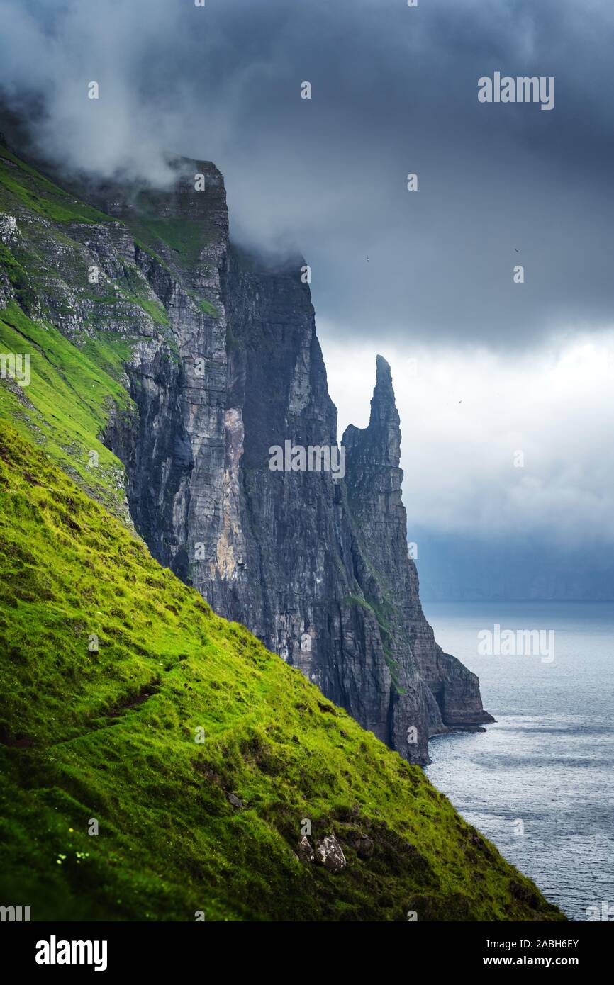 Splendido panorama delle isole Faeroeer con il famoso streghe dito scogliere e drammatico cielo nuvoloso dal punto di vista Trollkonufingur. Funzionario Ministeriale isola, isole Faerøer, Danimarca. Foto Stock