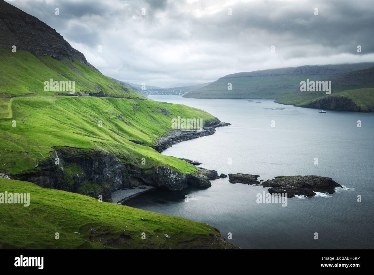 Drammatica vista delle verdi colline del funzionario ministeriale isola e Sorvagur città sullo sfondo. Isole Faerøer, Danimarca. Fotografia di paesaggi Foto Stock