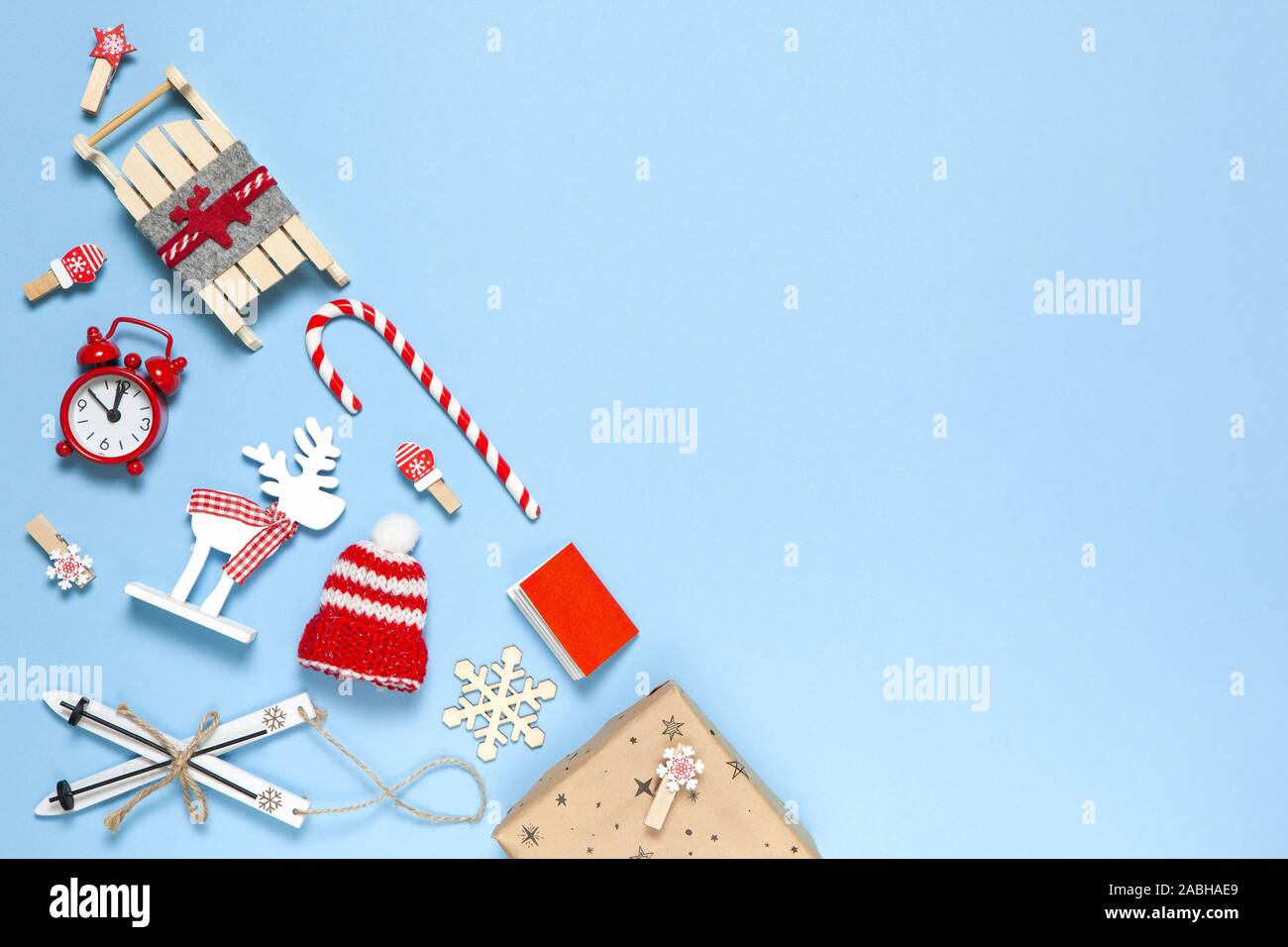 Angolo creativo di composizione di Natale. Candy Cane, dono, sled, cervi, cappello, sveglia, sci, clothespins, libro, fiocchi di neve in legno su sfondo blu, c Foto Stock