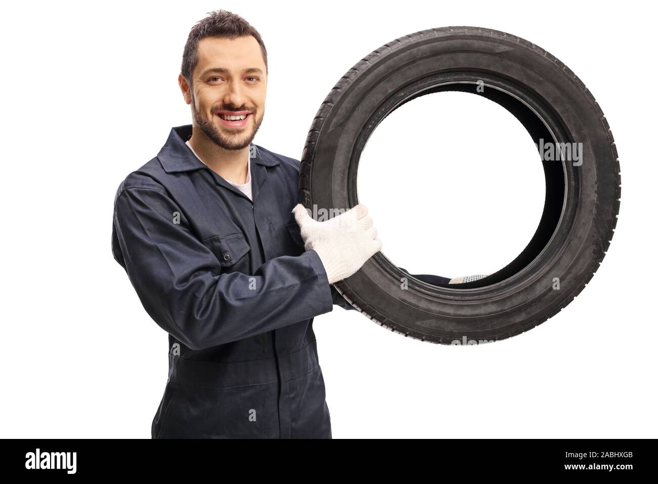 Meccanico automatico tenendo un pneumatico per automobile e sorridente alla telecamera isolata su sfondo bianco Foto Stock