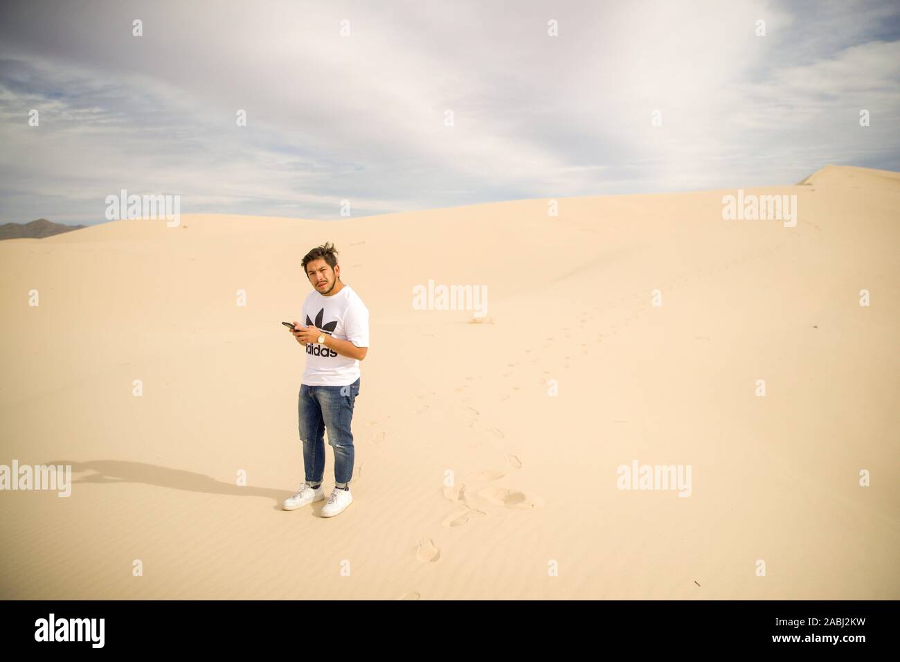 Un uomo obcervates il suo telefono cellulare, smartphone nelle dune di sabbia del deserto Samalayuca, Chihuahua in Messico. 52 km a sud di Ciudad Juárez in medio o Foto Stock