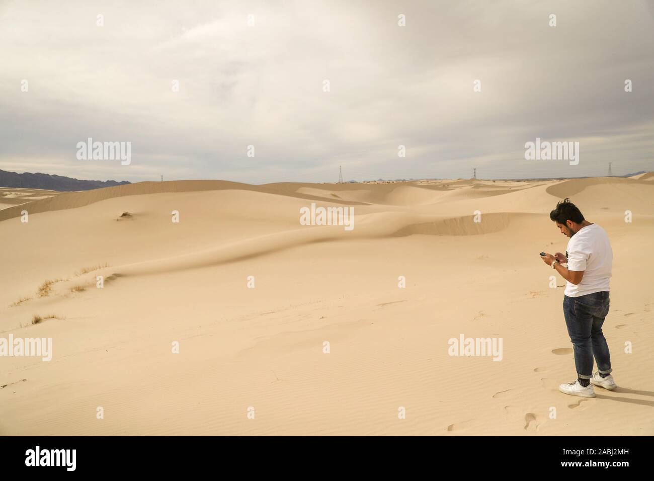 Un uomo obcervates il suo telefono cellulare, smartphone nelle dune di sabbia del deserto Samalayuca, Chihuahua in Messico. 52 km a sud di Ciudad Juárez in medio o Foto Stock
