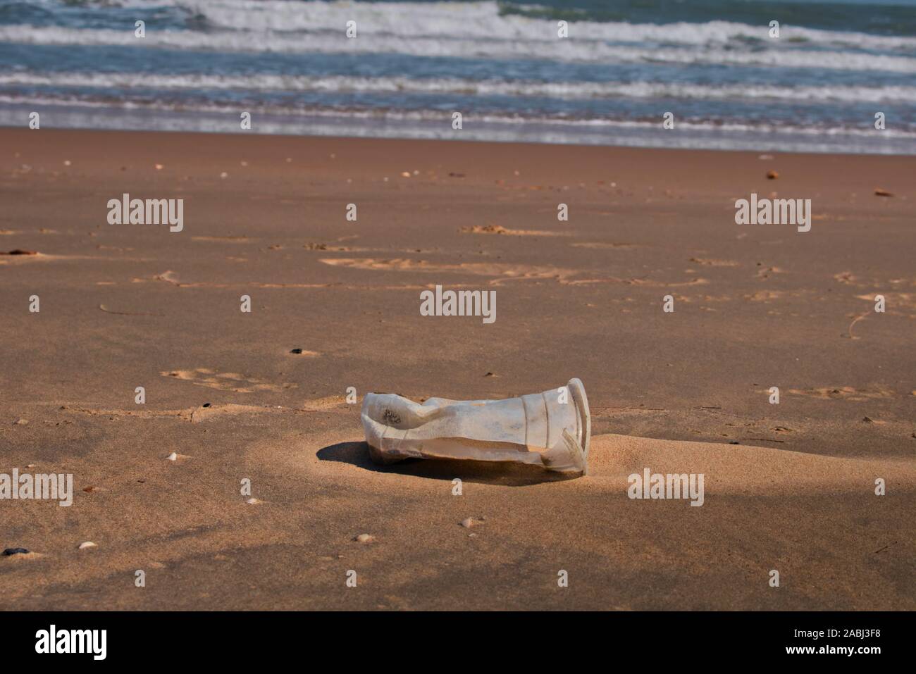 Questa foto unica mostra una tazza di plastica scartata che è stata lavata dal mare alla spiaggia Foto Stock