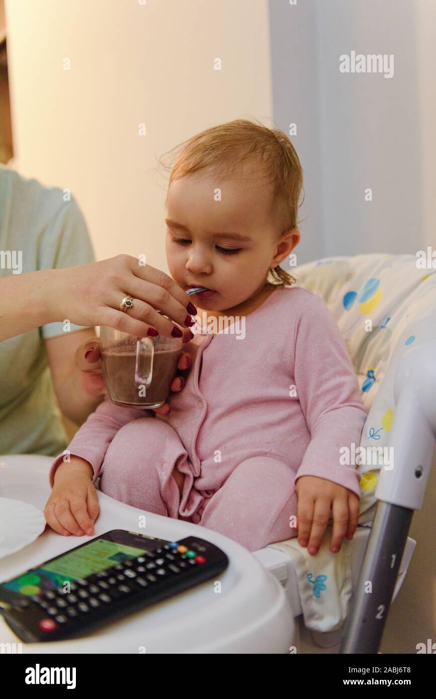 Carino bambino biondo si siede in un seggiolino per bambino in cucina a mangiare una succosa pesca. Bambina con un piercing look. Foto Stock