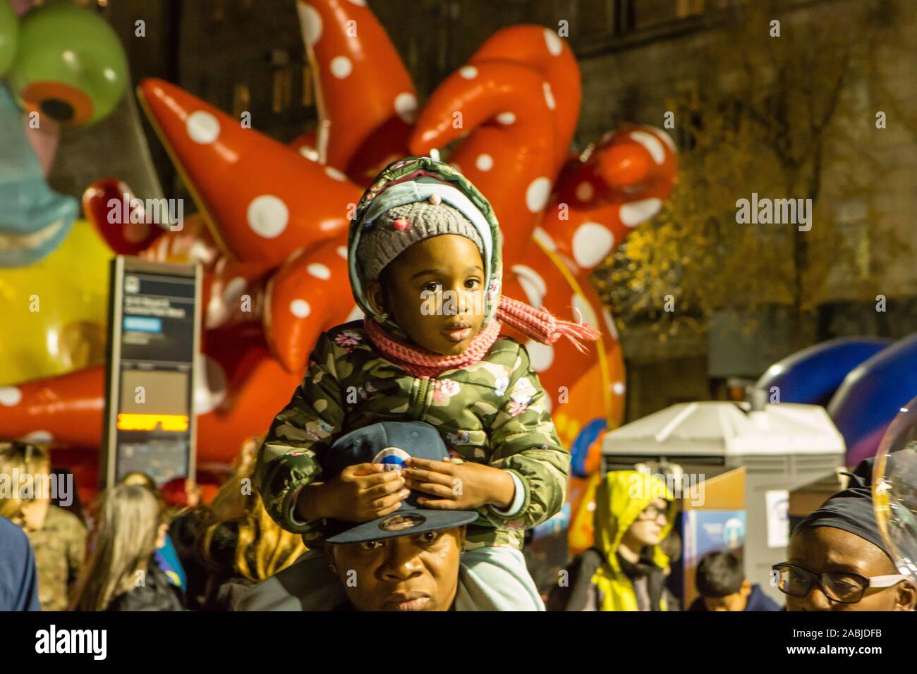 New York, NY, STATI UNITI D'AMERICA. 27 Nov, 2019. Migliaia di spettatori pranzo le strade intorno al Museo Americano di Storia Naturale per vedere la zona di gonfiaggio per i palloncini per Macy's Thanksgiving Day Parade. Una ragazza corre sul suo padre le spalle di fronte di Yayoi Kusama 'amore vola fino al cielo.' Credit: Ed Lefkowicz/Alamy Live News Foto Stock