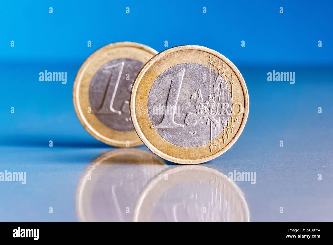 Due piedi graffiato un conio di monete metalliche in euro su un blu sfondo riflettente con riflessioni di monete Foto Stock