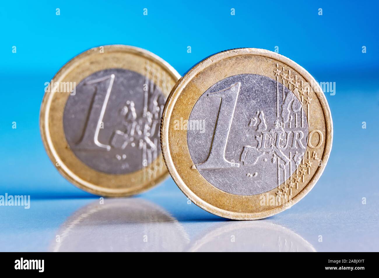 Due piedi graffiato un conio di monete metalliche in euro su un blu sfondo riflettente con riflessioni di monete Foto Stock
