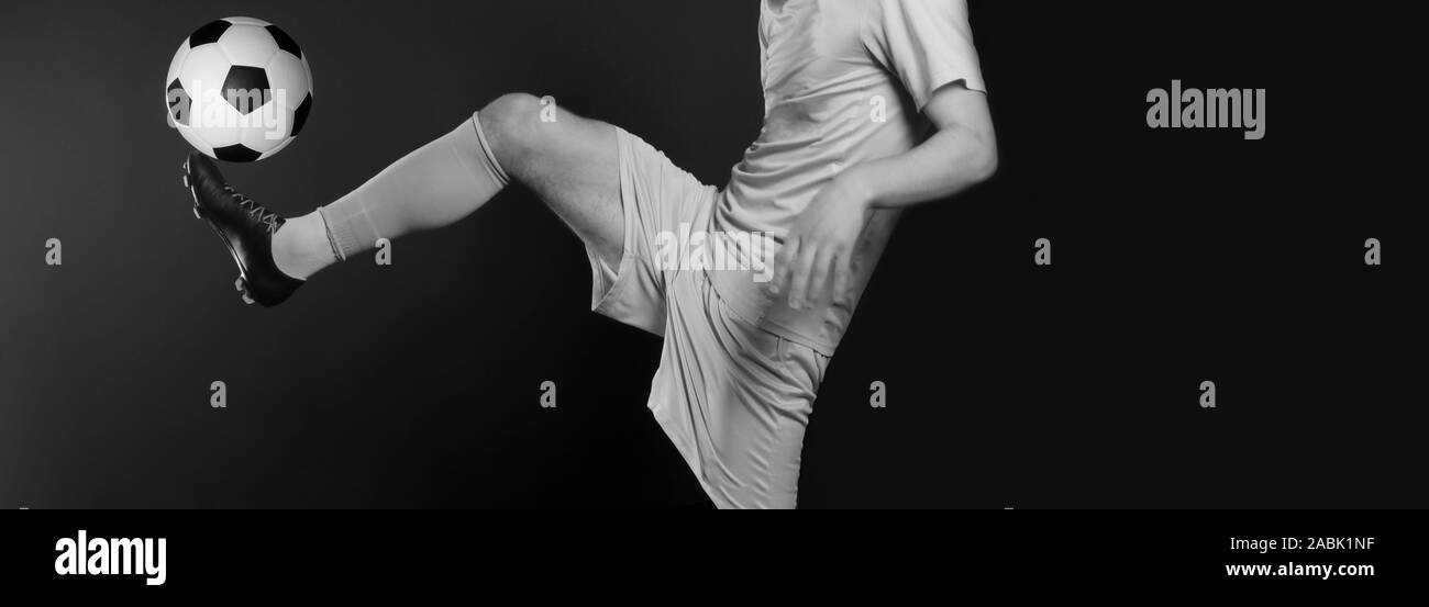 Chiudere le gambe e la scarpa da calcio del giocatore di football in azione calci palla isolati su sfondo nero. In bianco e nero il filtro Foto Stock