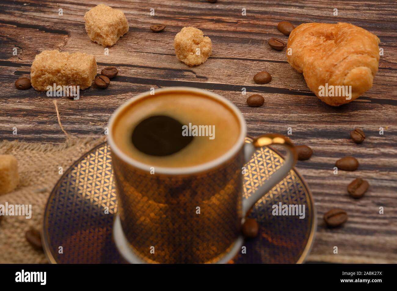 Tazza da caffè, croissant, lo zucchero di canna e i chicchi di caffè su sfondo di legno. Close up Foto Stock
