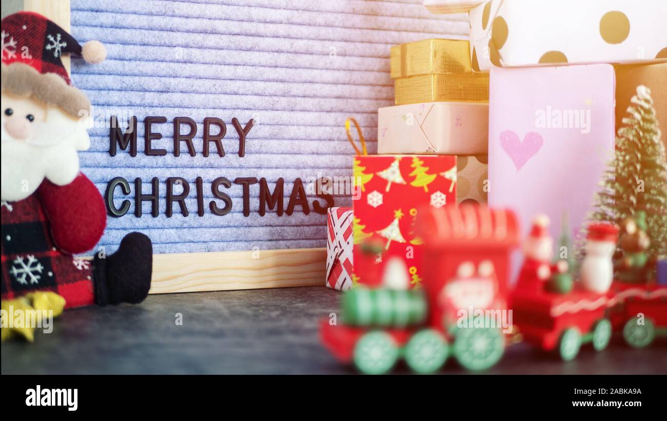 Testo BUON NATALE sulla lettera di bordo su tavola, decorata con ornamento di Natale , confezione regalo presente e Santa Claus bambola. messa a fuoco selettiva Foto Stock