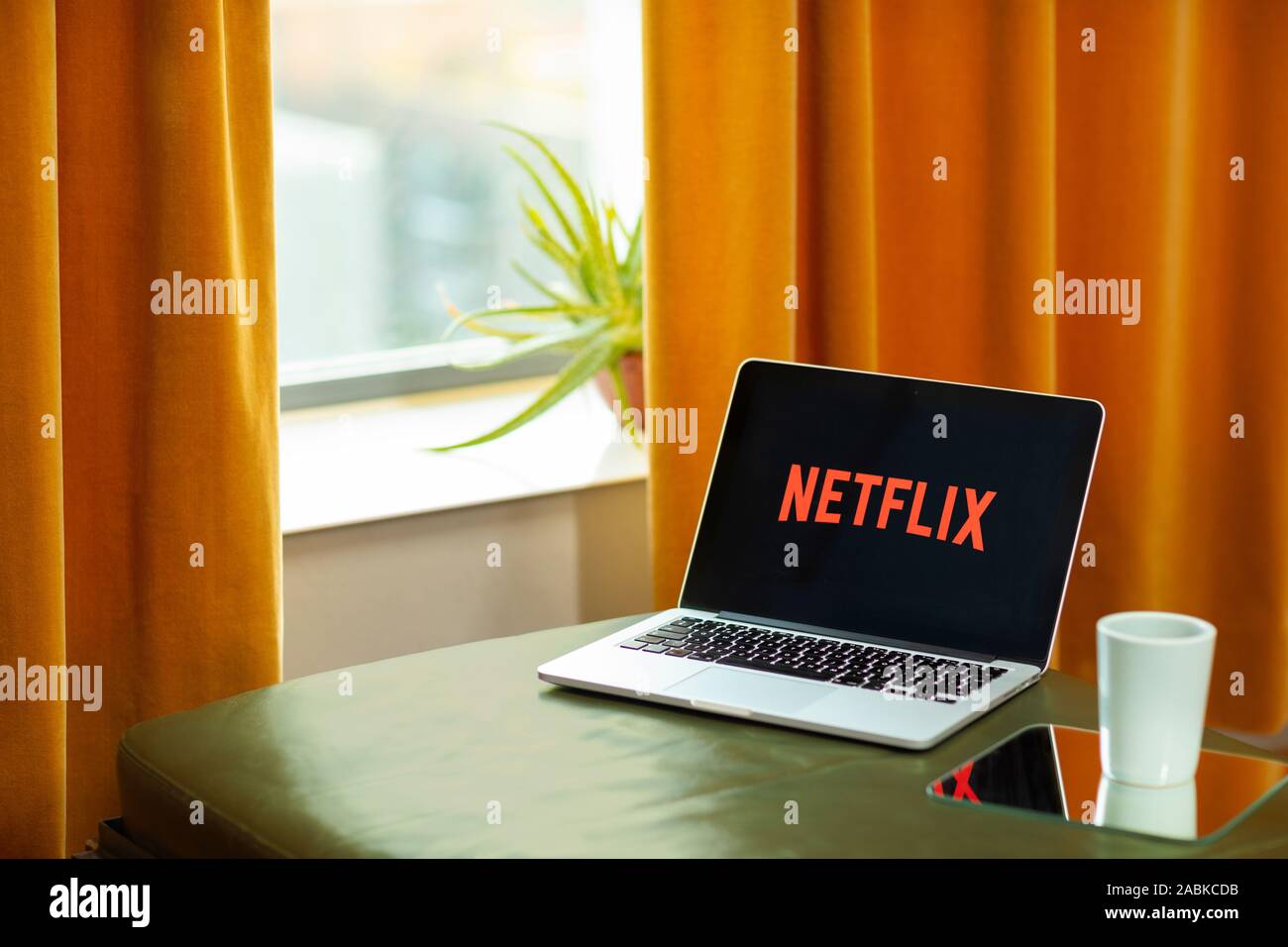 Eindhoven, Paesi Bassi, 20 giugno 2019. Guardando l'account Netflix logo su un laptop macbook posa su un lettino di verde e di una cortina di arancione, retro Foto Stock