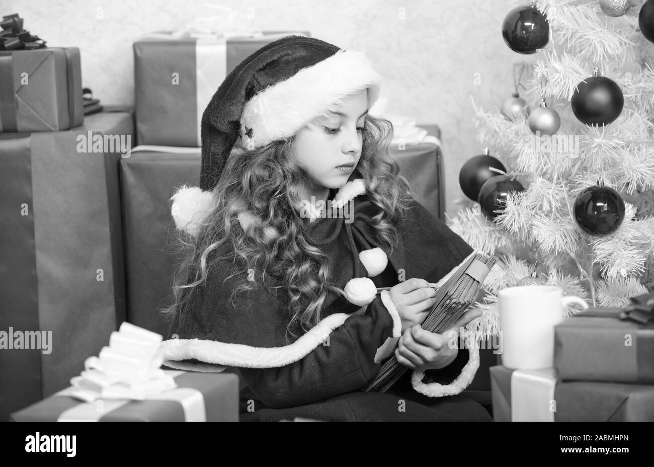 Ragazza tenete la penna e la carta vicino a albero di natale e la confezione regalo. Credere nel miracolo. Inviare una lettera per santa. La lista dei desideri. Bambino santa costume godetevi la vigilia di Natale. Bambino di scrivere la lettera a Babbo Natale. Cari santa. Foto Stock