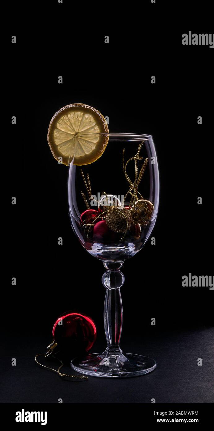 Silhouette luminose di un vetro con una fettina di limone e il rosso del Natale e del nuovo anno sfera isolata su uno sfondo scuro. Modalità Buia Foto Stock