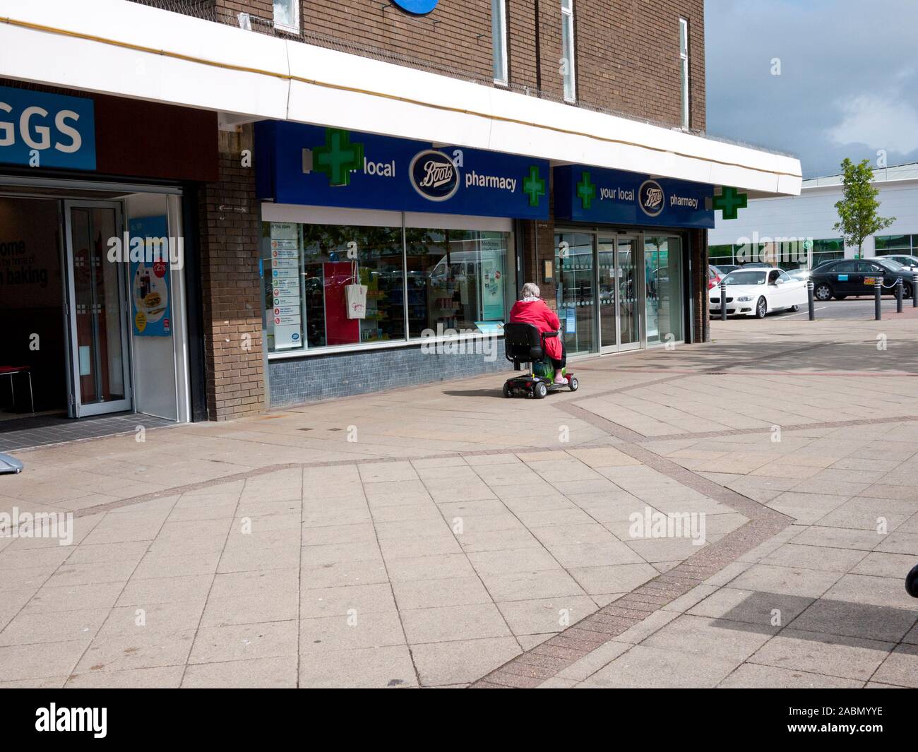 Lady in buggy mobilità passando Boots Pharmacy Chadderton, Oldham, Lancashire, Regno Unito. Foto Stock