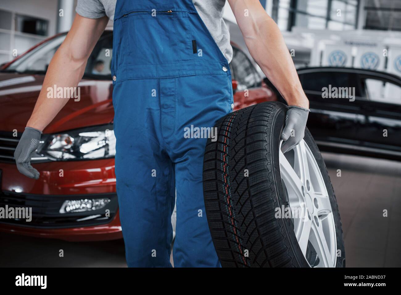 Mechanic tenendo un pneumatici presso il garage di riparazione. sostituzione delle gomme invernali ed estive Foto Stock