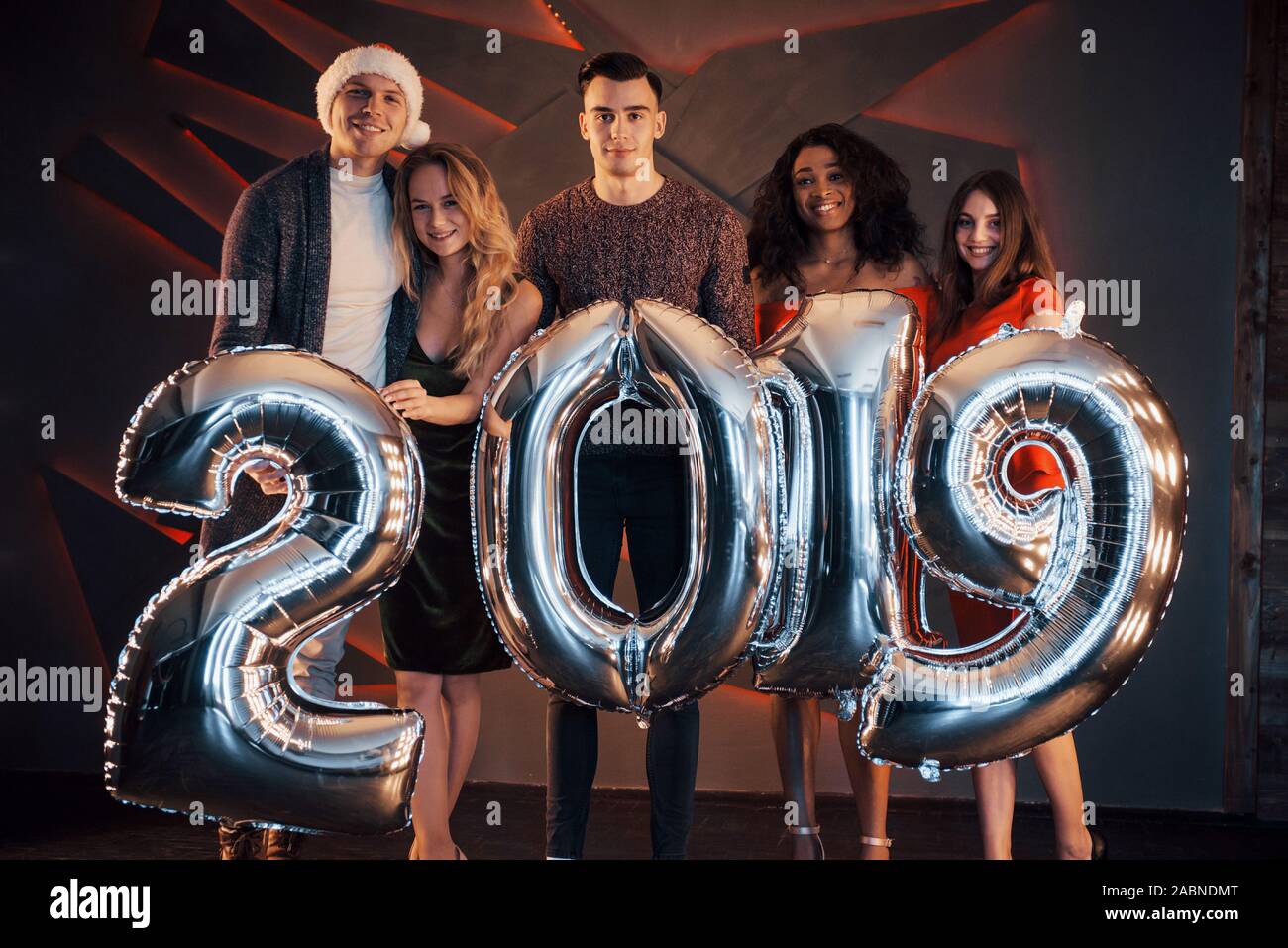 Il nuovo 2019 si avvicina. Un gruppo di giovani allegri gente multinazionale in Santa's hat con numeri di argento e gettando i confetti al partito. Felice Foto Stock